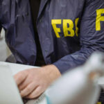 Person in FBI jacket typing on laptop