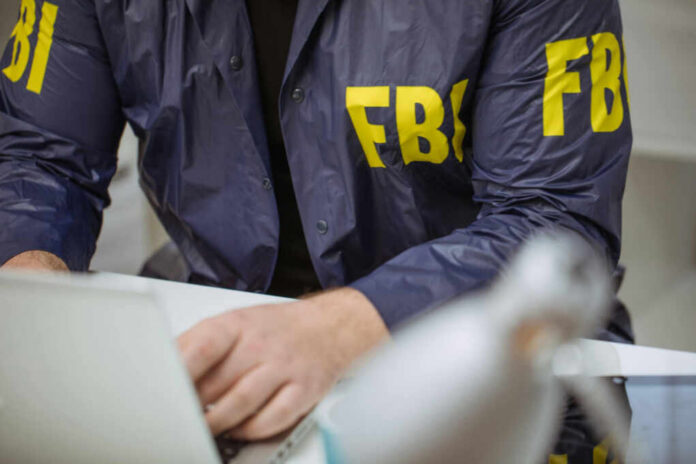 Person in FBI jacket typing on laptop