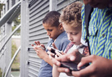 Three children focused on their smartphones while standing outdoors