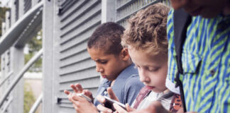 Three children focused on their smartphones while standing outdoors