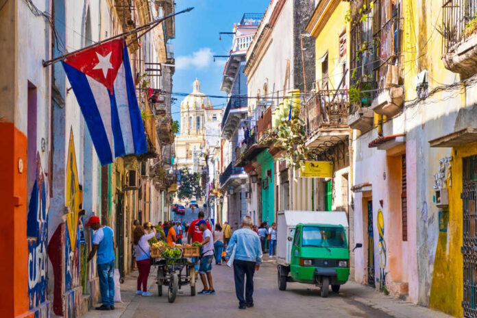 Colorful street scene with Cuban flag and people.