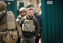 Men in military gear in front of green gate.