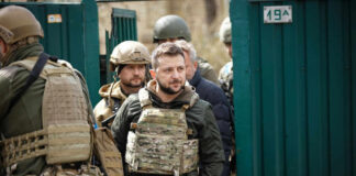 Men in military gear in front of green gate.