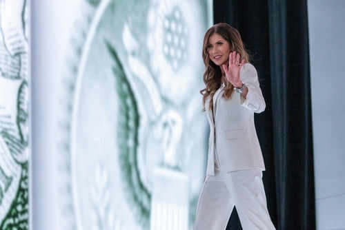 Kristi-Noem_2519820601 Person in white suit waves on stage background