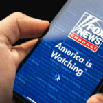 LIVE Suplex Shocker: Fox’s Hornacek Smiles Through It Hand holding smartphone showing Fox News Channel logo.