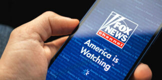 Hand holding smartphone showing Fox News Channel logo.