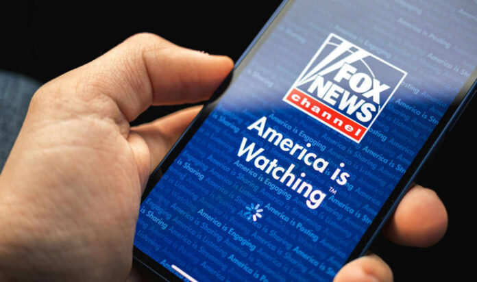 Hand holding smartphone showing Fox News Channel logo.
