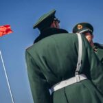Two Chinese soldiers in uniform standing near the national flag