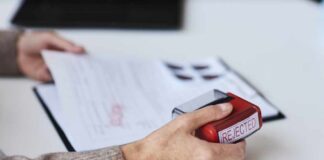 A hand holding a red stamp labeled 'REJECTED' over a document