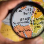 Iran’s Proxy Menace: Houthis Fire on Israel A hand holding a magnifying glass over a map focusing on Israel