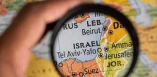 A hand holding a magnifying glass over a map focusing on Israel