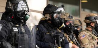 Police officers in tactical gear and gas masks standing in formation