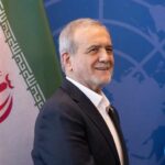A man smiling in front of flags at a diplomatic event