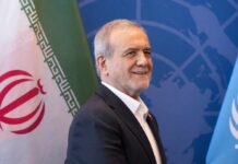 900-Strike Blitz ROCKS Iran Overnight A man smiling in front of flags at a diplomatic event