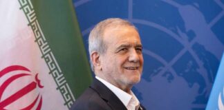 A man smiling in front of flags at a diplomatic event
