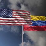 Flags of the United States and Venezuela waving against a cloudy sky