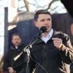 A speaker addressing an audience at an outdoor event with a microphone