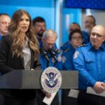 A woman speaking at a podium during a press conference with government officials in the background