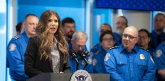 A woman speaking at a podium during a press conference with government officials in the background