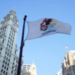 Illinois state flag waving in front of historic buildings against a blue sky