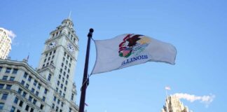 Illinois state flag waving in front of historic buildings against a blue sky