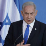 Netanyahu’s U-Turn After Trump Call Man speaking in front of Israeli flag backdrop