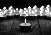 Eviction Horror: Detective Gunned Down Single candle burning among many on wooden surface.