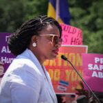 A woman speaking at a protest with signs advocating for abortion rights in the background