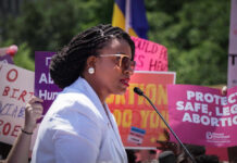 A woman speaking at a protest with signs advocating for abortion rights in the background