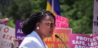 A woman speaking at a protest with signs advocating for abortion rights in the background