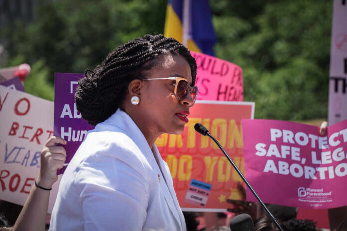 A woman speaking at a protest with signs advocating for abortion rights in the background