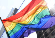 A vibrant rainbow flag waving against a city backdrop