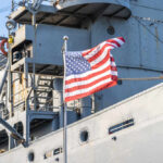 American flag waving in front of a naval ship