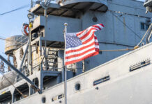 American flag waving in front of a naval ship