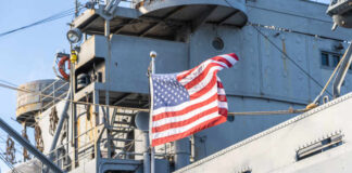 American flag waving in front of a naval ship