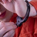 Person in an orange jumpsuit attempting to unlock handcuffs