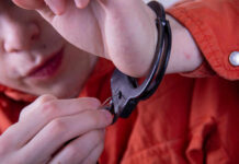 Person in an orange jumpsuit attempting to unlock handcuffs