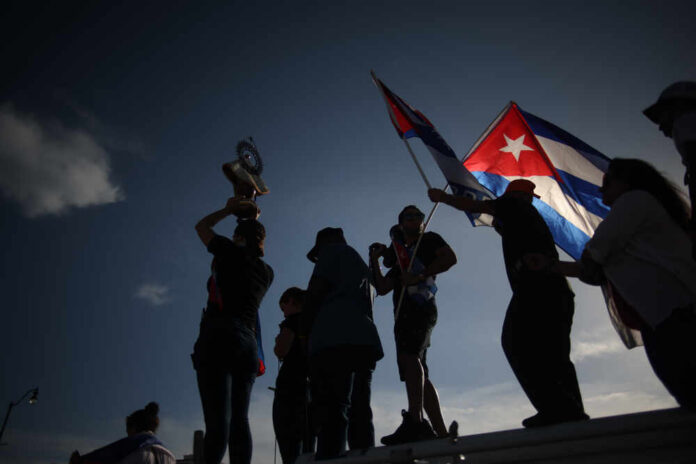 shutterstock_2006478167.jpg Silhouetted figures holding a trophy and Cuban flags during a celebration