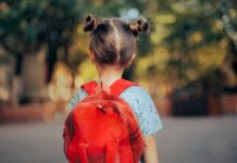 A young child with a red backpack seen from behind, standing outdoors