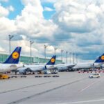 Several Lufthansa airplanes parked at an airport under a cloudy sky