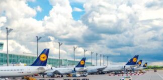 Several Lufthansa airplanes parked at an airport under a cloudy sky