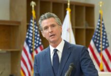 A government official speaking at a podium with American flags in the background