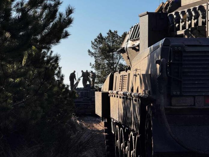 shutterstock_2596334357.jpg Silhouette of soldiers near a military vehicle in a wooded area