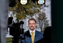 A man in a suit standing in front of a camera during a news broadcast