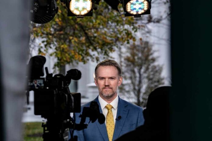 A man in a suit standing in front of a camera during a news broadcast