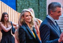 Two individuals in formal attire at a red carpet event, with others in the background