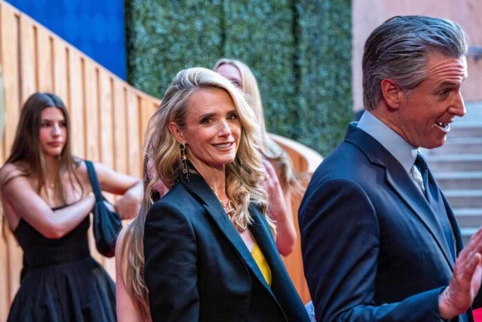 Two individuals in formal attire at a red carpet event, with others in the background