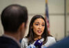 Person speaking to reporters with microphones indoors