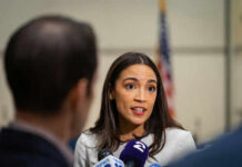 Person speaking to reporters with microphones indoors
