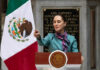 Person speaking at podium with Mexican flag nearby